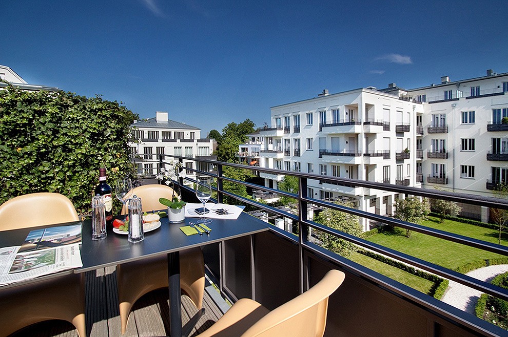 Gedeckter Tisch auf einem Balkon mit Blick auf den begrünten Innenhof und die weißen Wohnhäuser