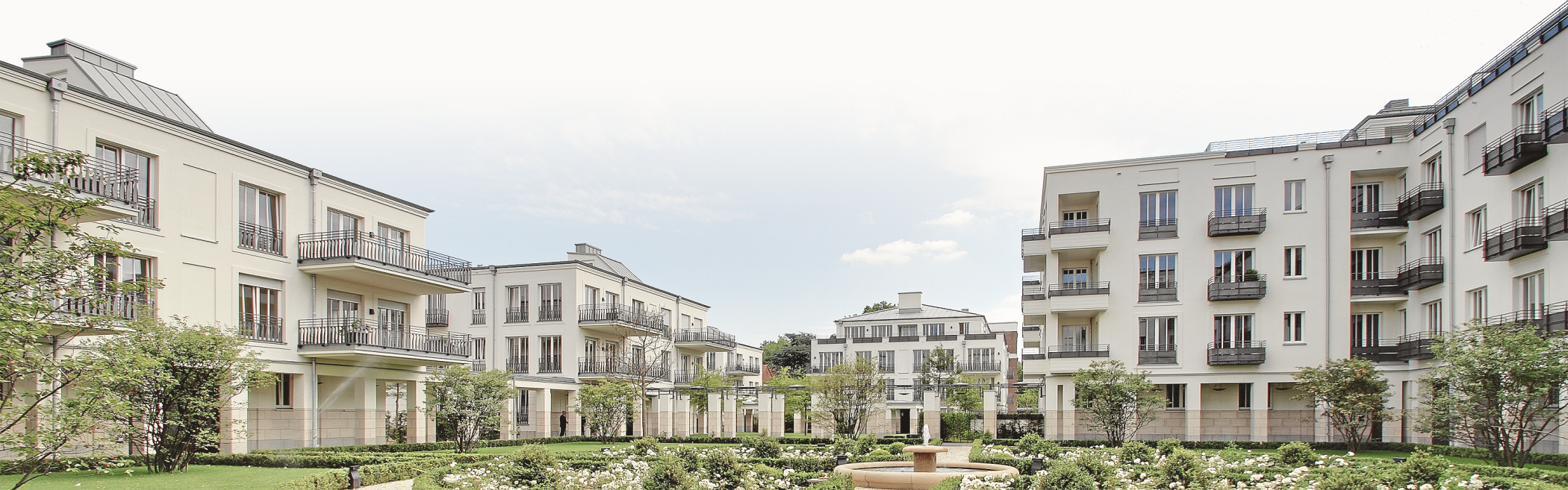 Panoramablick über den Innenhof mit Gartenanlage und hellen Wohnhäusern unter leicht bewölktem Himmel