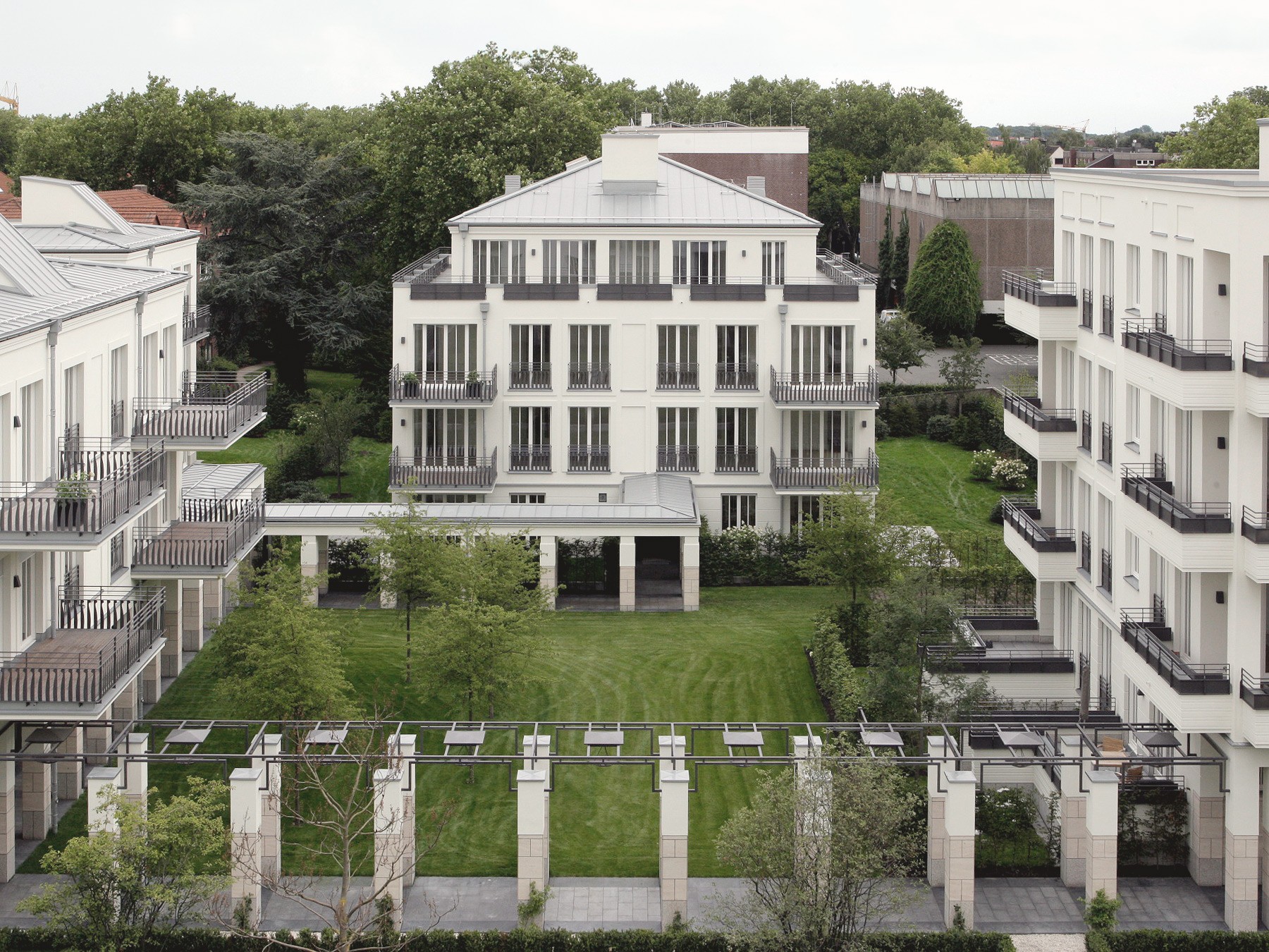 Blick von oben auf den Gartenhof mit Pergola und Rasen, umgeben von hellen Wohnhäusern und altem Baumbestand